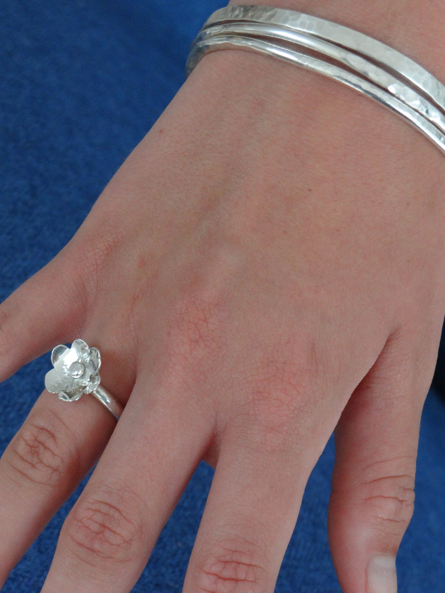 Model wearing handmade sterling silver flower ring and hammered bangles