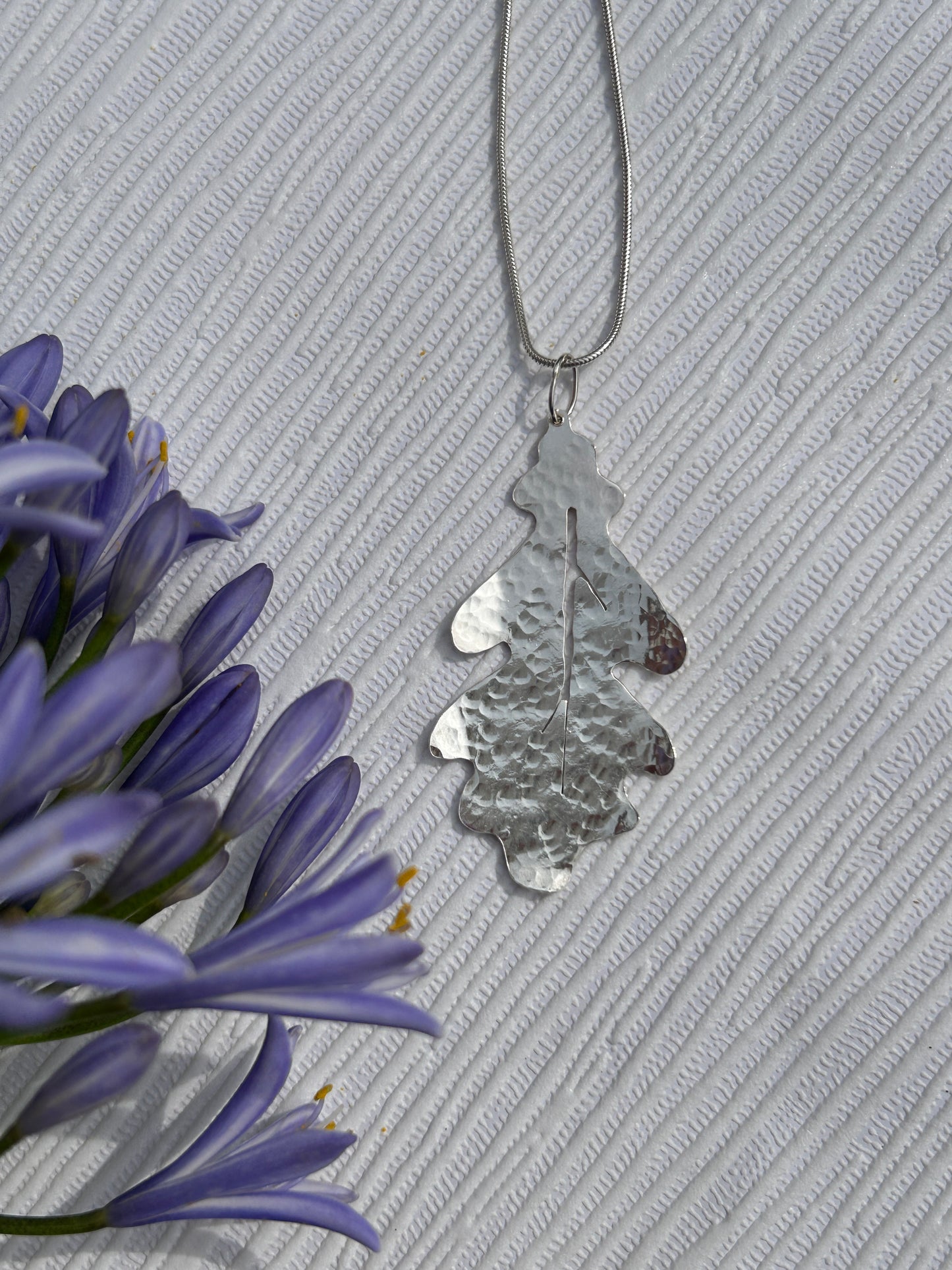 Handcrafted sterling silver pendant in the shape of an oak leaf with a hammered texture hanging on a silver chain
