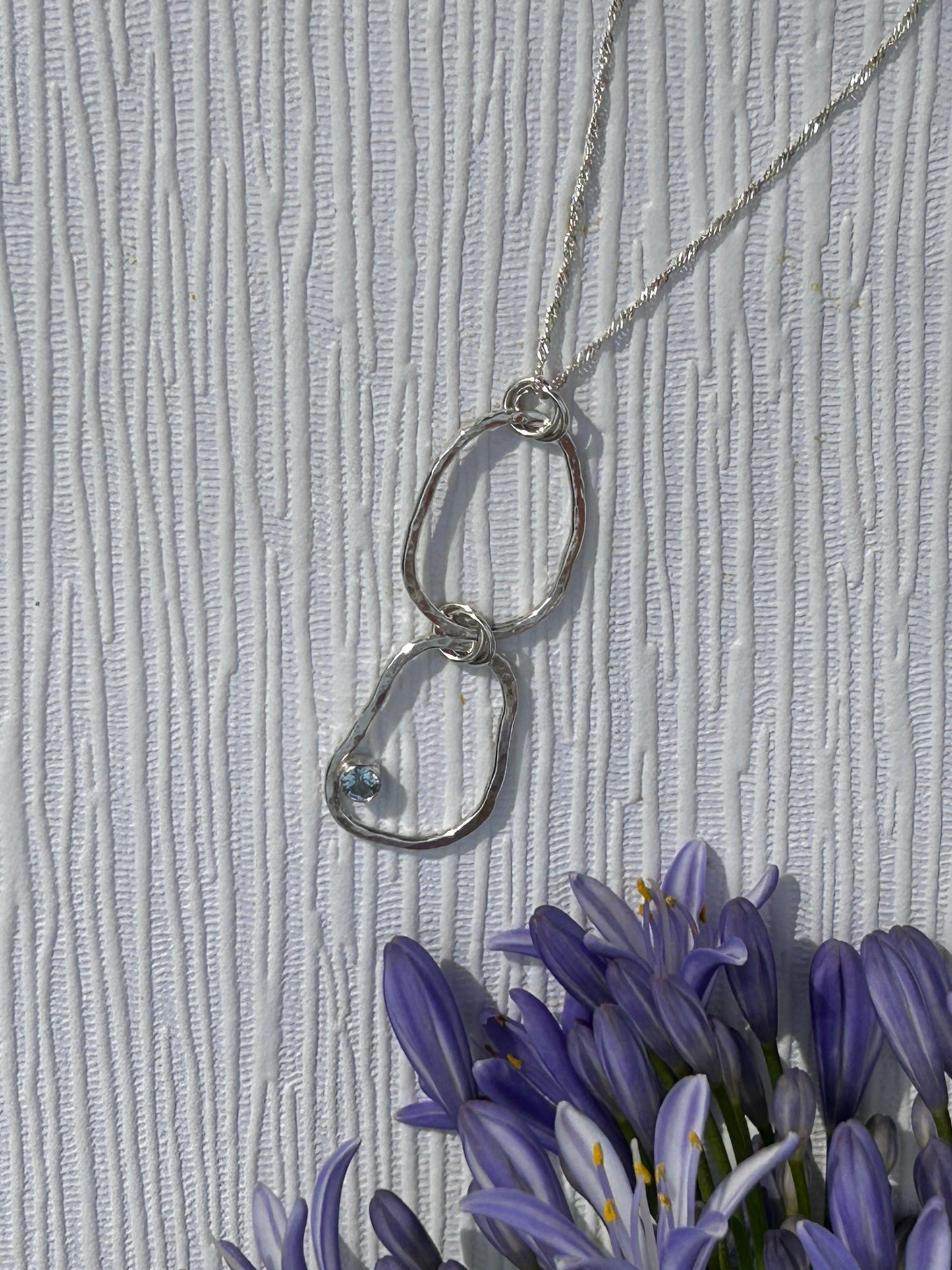 Handmade sterling Silver pendant necklace with interlocking rings with blue topaz gemstone hanging on a delicate silver chain.  