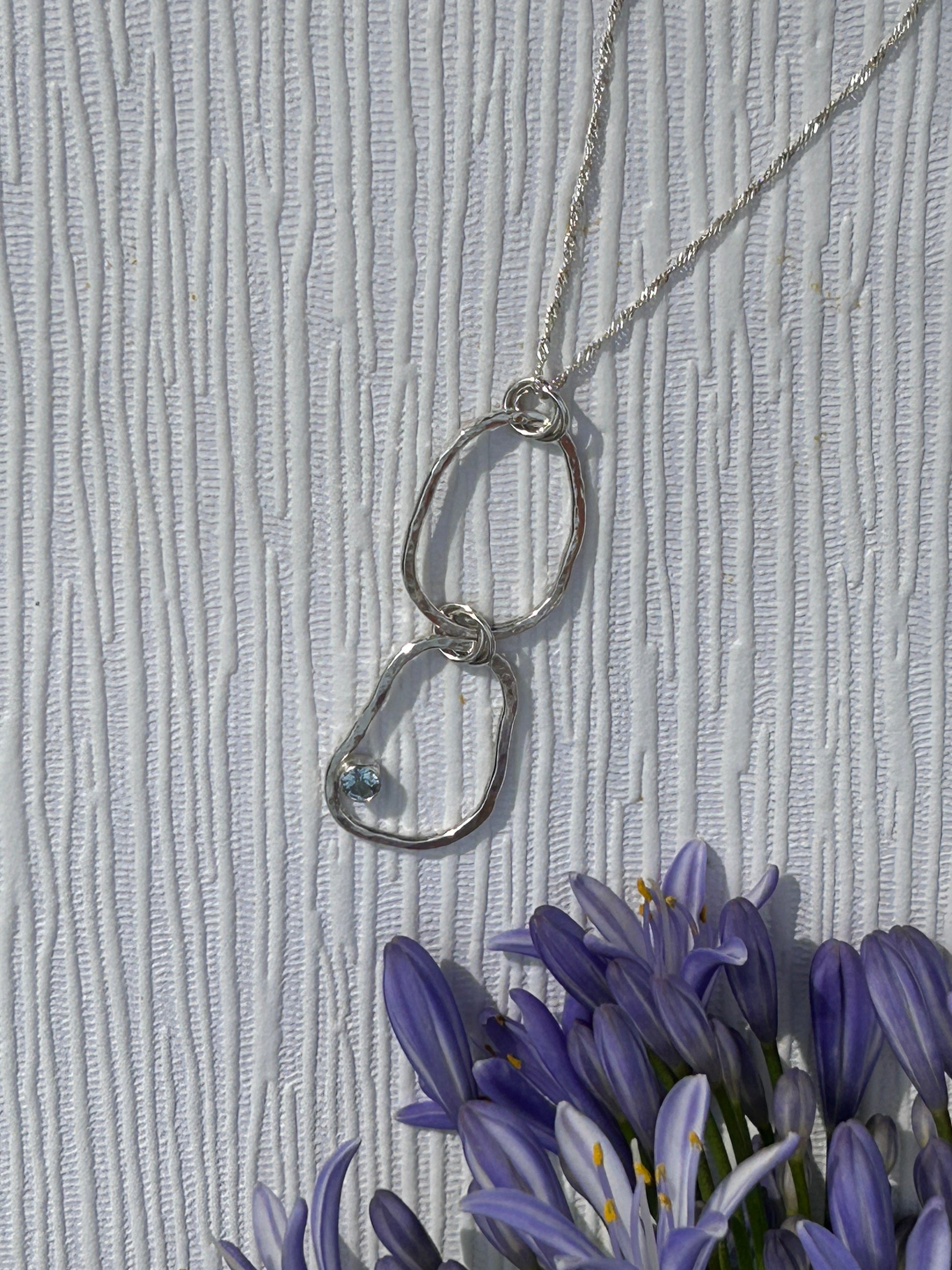 Handmade sterling Silver pendant necklace with interlocking rings with blue topaz gemstone hanging on a delicate silver chain.  