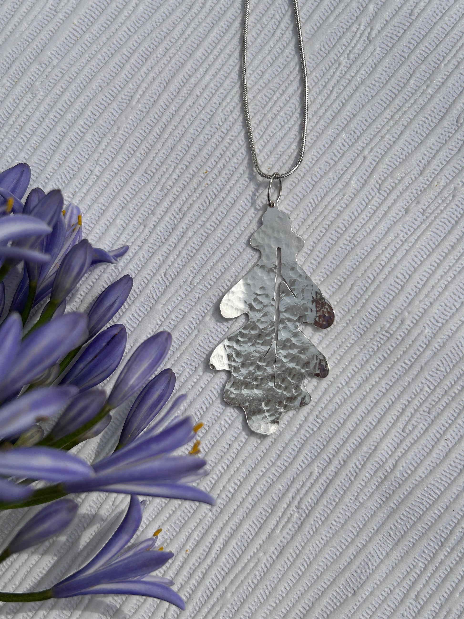 Handcrafted sterling silver pendant in the shape of an oak leaf with a hammered texture hanging on a silver chain