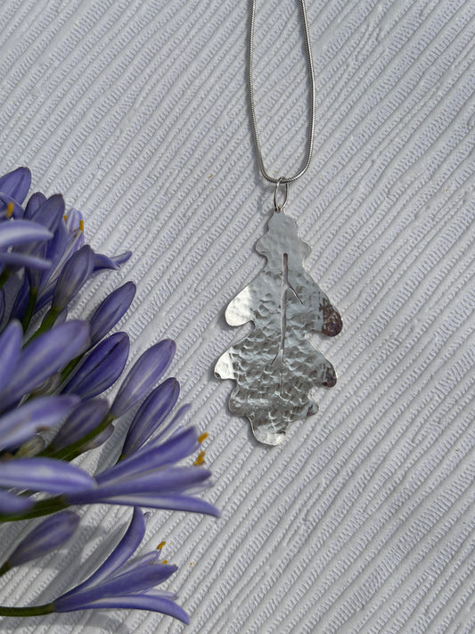 Handcrafted sterling silver pendant in the shape of an oak leaf with a hammered texture hanging on a silver chain